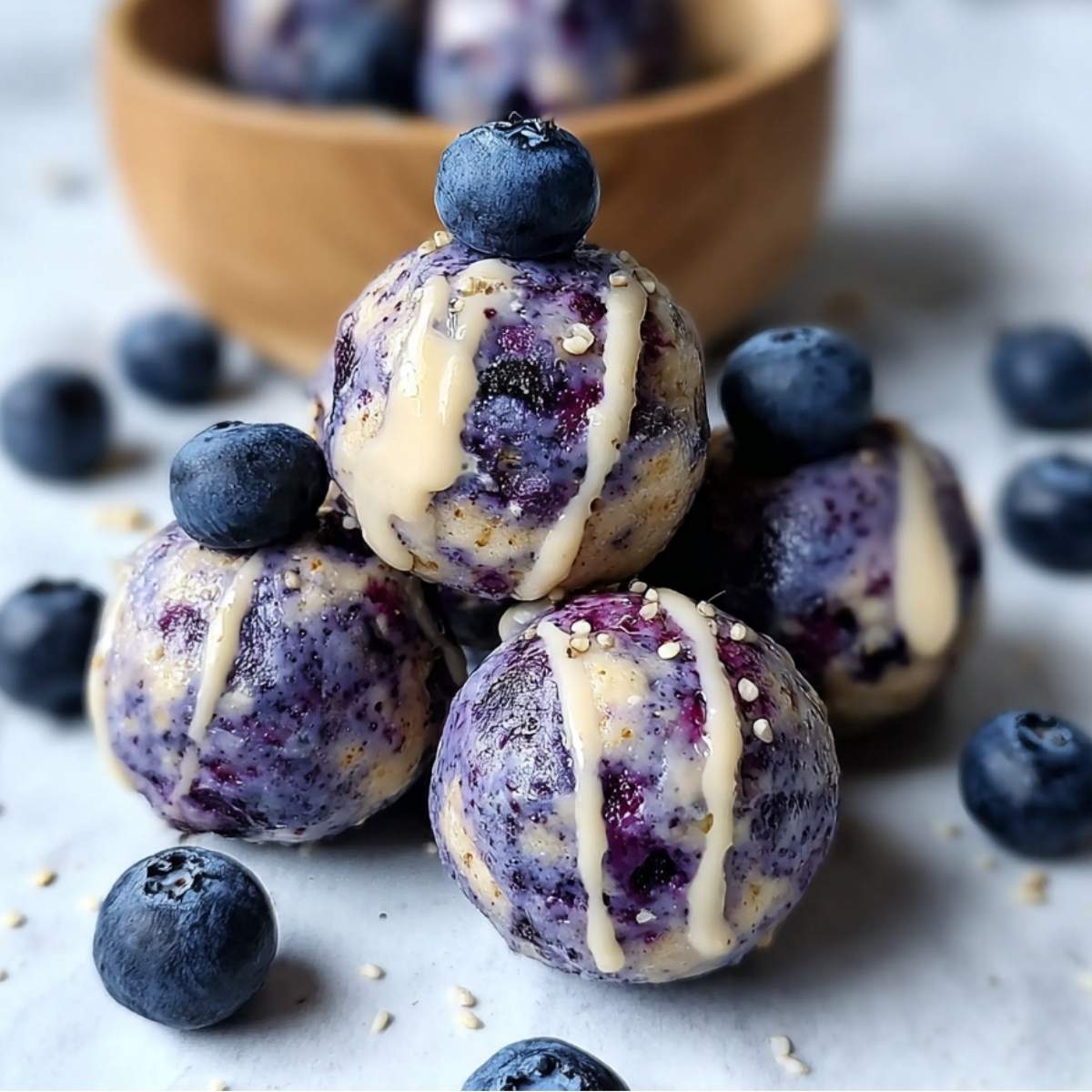 Blueberry Cheesecake Protein Bites on a modern marble countertop, showcasing their creamy drizzle and fresh blueberries