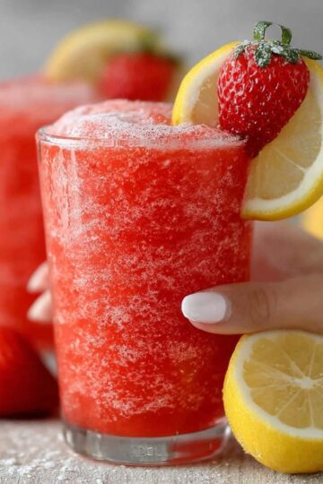 Close-up of Frozen Strawberry Lemonade showing icy slushy texture and vibrant red color, garnished with fresh strawberry and lemon slice.