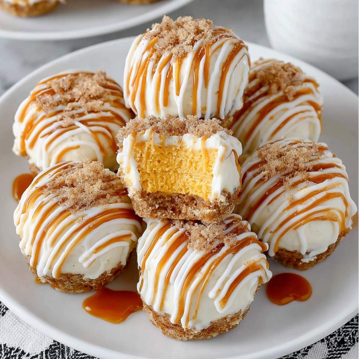 Pumpkin Spice Cheesecake Bites featuring a visible graham cracker crust base, white chocolate drizzle, and caramel sauce on a white plate