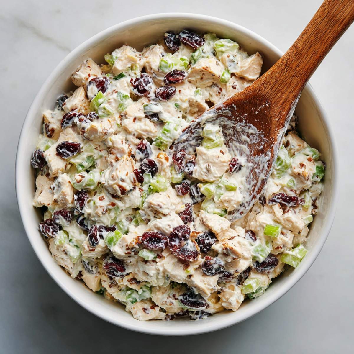 Close-up of Easy Chicken Salad Recipe showing creamy chicken pieces with celery and dried cranberries in a white bowl.