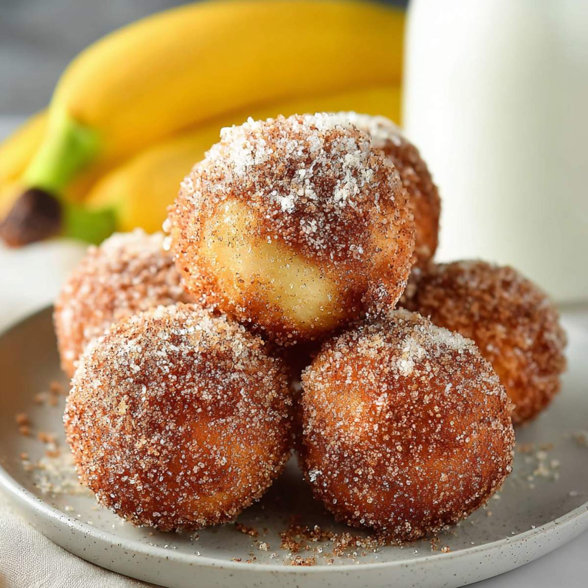 Close-up of 2-Ingredient Banana Donut Holes showing fluffy banana interior and golden cinnamon sugar crust on a white plate.