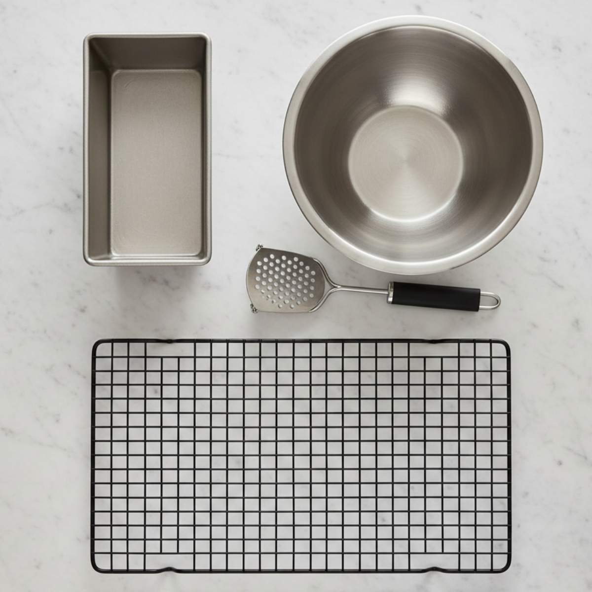 Essential equipment for chocolate chip banana bread including a 9x5 loaf pan, mixing bowl, potato masher, and wire cooling rack