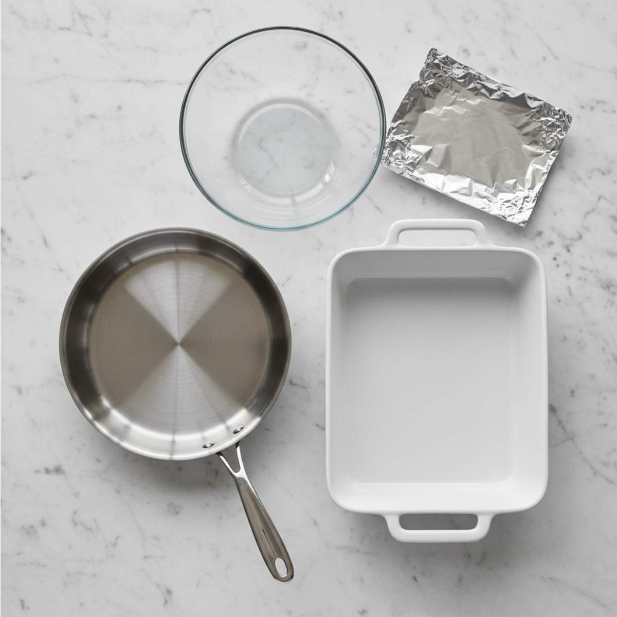 Cooking equipment for Crack Breakfast Casserole including skillet, mixing bowl, foil, and baking dish on a marble countertop.