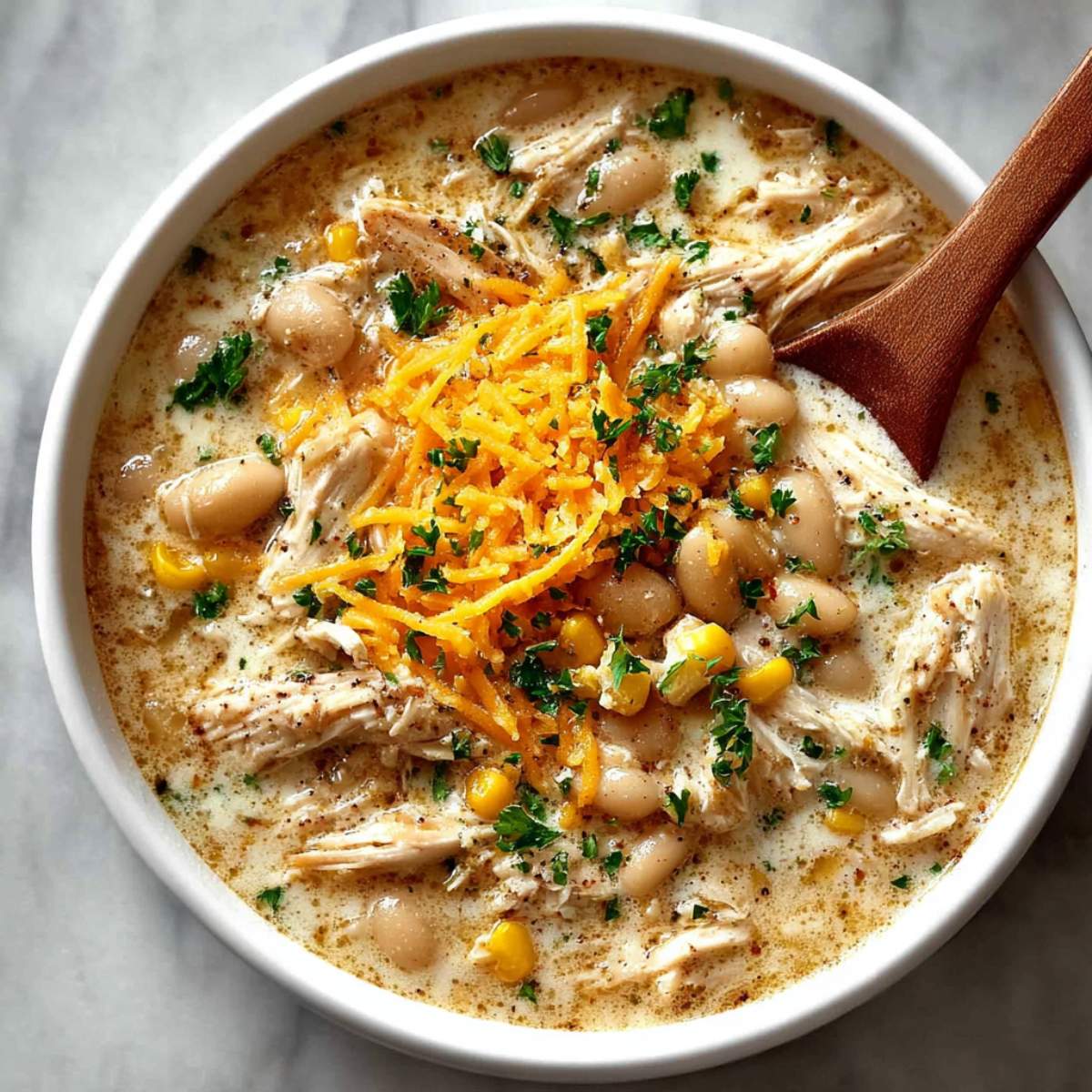White chicken chili in a ceramic bowl, showcasing creamy broth, shredded chicken, white beans, corn, and melted cheddar cheese