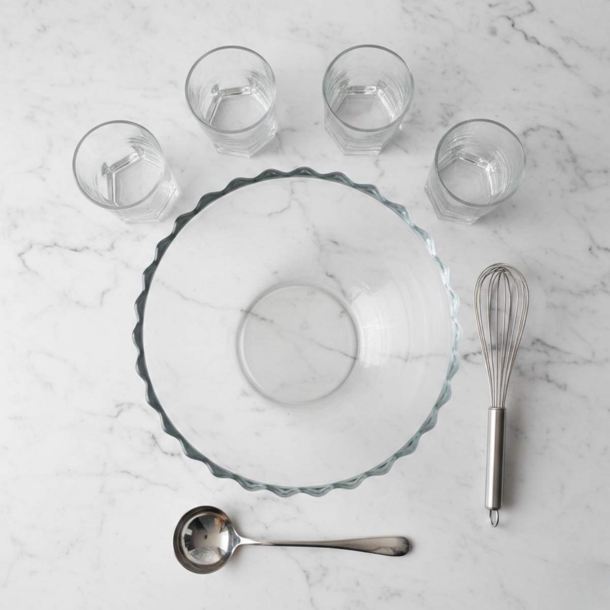 Glass punch bowl, whisk, ladle and serving glasses arranged for making non alcoholic pina colada punch recipe at home easil