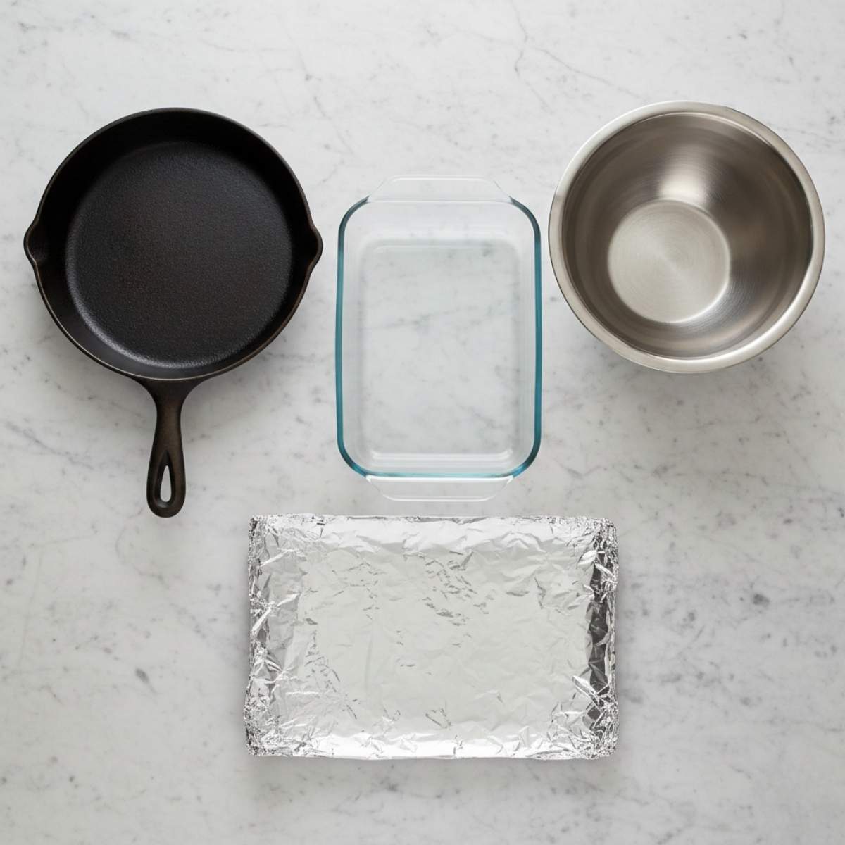 Essential kitchen equipment for Million Dollar Lasagna including skillet, mixing bowl, baking dish, and foil on marble surface.