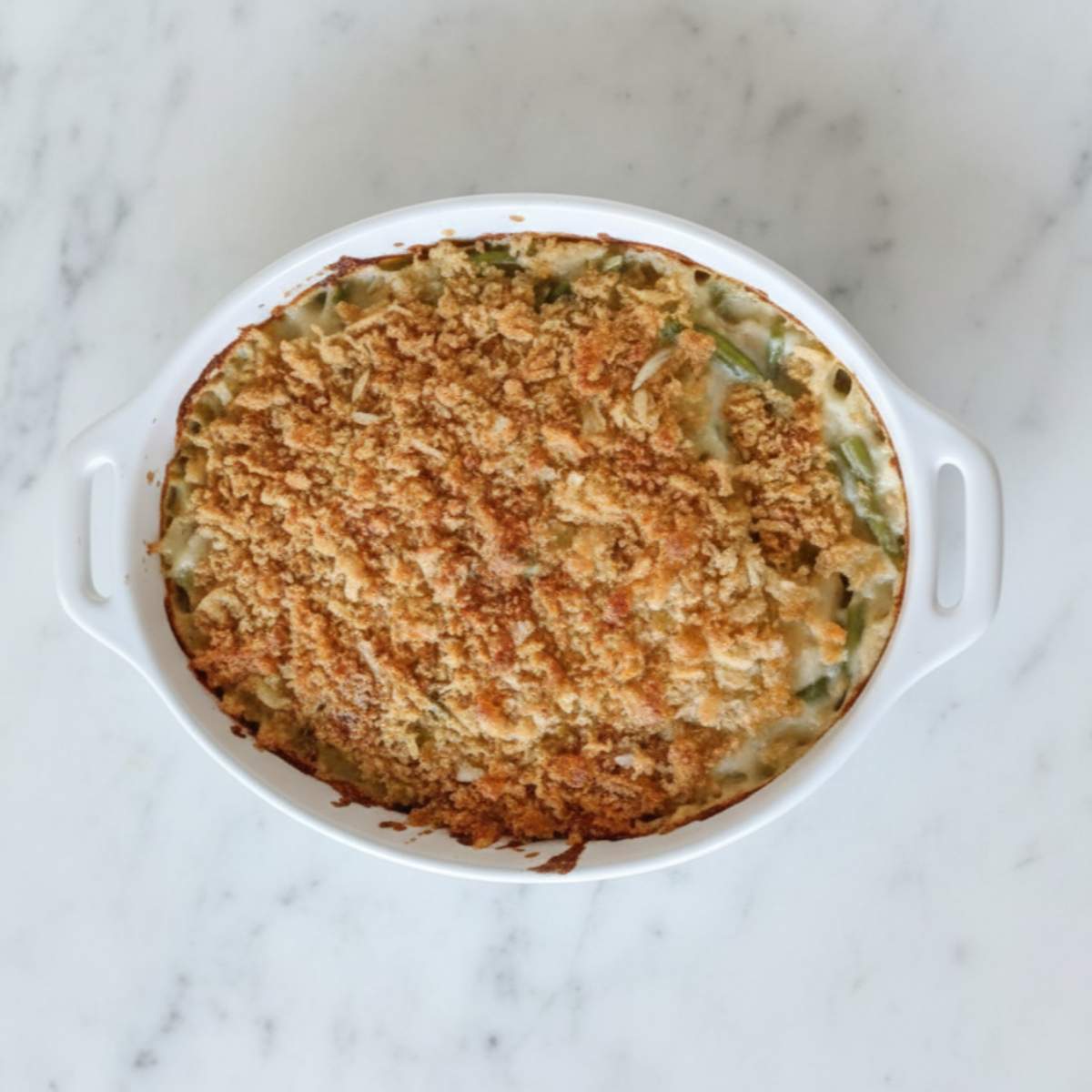 Southern Green Bean Casserole in a white baking dish, topped with golden crispy onions and creamy green beans on marble countertop
