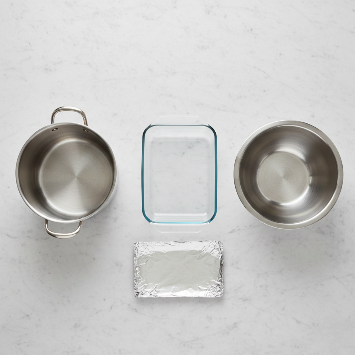 Equipment for spinach and ricotta stuffed shells including pot, glass baking dish, metal mixing bowl and foil pan on marble surface.
